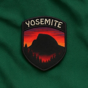 May include: Embroidered patch with the word "YOSEMITE" above a mountain silhouette at sunset. The patch has a black border and is set against a green fabric background.