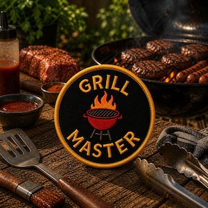May include: A round black patch with the words "GRILL MASTER" embroidered in yellow, featuring a red grill graphic with flames. The patch is on a wooden surface with grilling tools, a grill with burgers, and other barbecue items.