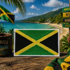 May include: A rectangular embroidered patch of the Jamaican flag, featuring a green field with a yellow diagonal cross and black triangles. A mug with "JAMAICA" printed on it and a flag waving in the background. The scene is set on a wooden surface.