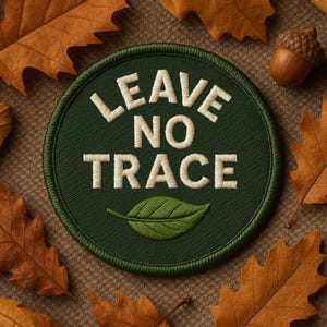 Może przedstawiać: Okrągła zielona naszywka z białym napisem "LEAVE NO TRACE" i zielonym motywem liścia. Naszywka otoczona jest zieloną obwódką i umieszczona na brązowym tle z jesiennymi liśćmi i żołędziem.