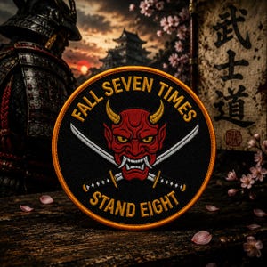May include: A circular embroidered patch featuring a red oni mask with yellow horns and two crossed silver katanas. The text "FALL SEVEN TIMES" is arched above the mask, and "STAND EIGHT" is arched below, all in yellow thread on a black background.