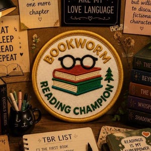 Peut inclure: Un écusson brodé circulaire à fond blanc avec une bordure dorée. Le motif représente une pile de livres rouges et verts surmontée de lunettes noires, entourée du texte BOOKWORM READING CHAMPION et d'un petit sapin vert.