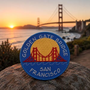 May include: A circular embroidered patch featuring a blue background with a yellow sun, a red Golden Gate Bridge illustration, and white waves. The text reads GOLDEN GATE BRIDGE and SAN FRANCISCO in white capital letters along the circular border.