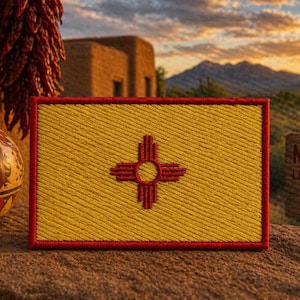 Puede incluir: Un parche rectangular bordado con el diseño de la bandera del estado de Nuevo México, que consiste en un campo amarillo con un símbolo solar Zia rojo en el centro, todo encerrado dentro de un borde grueso cosido en rojo.