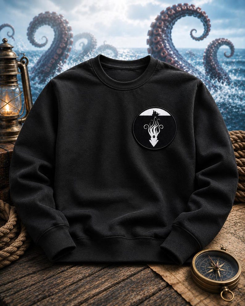 May include: A black crewneck sweatshirt featuring a circular patch on the left chest. The patch displays a white graphic of a sea creature with long tentacles extending downward from a small boat silhouette against a solid black background.