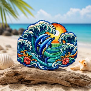 May include: An embroidered patch featuring two blue dolphins leaping through a large, stylized ocean wave. The design includes a bright yellow sun, swirling teal and navy water, and two red hibiscus flowers at the base, all rendered in vibrant thread.