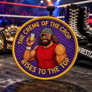 May include: A circular embroidered patch featuring a wrestler with long brown hair, a patterned headband, and colourful sunglasses, wearing a red tank top and holding a small white container. The text reads THE CRÈME OF THE CROP RISES TO THE TOP.