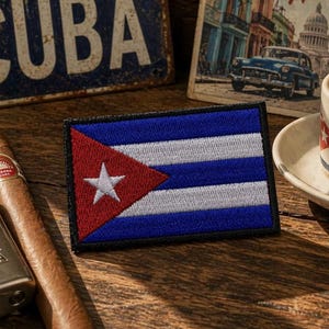 May include: A rectangular embroidered patch featuring the national flag of Cuba, which consists of three blue horizontal stripes, two white horizontal stripes, a red triangle on the left side, and a single white five-pointed star in the center.