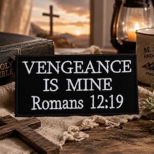 May include: A black patch with white embroidered text that reads "VENGEANCE IS MINE Romans 12:19." A wooden cross, a Bible, and a mug with the text "BE STILL AND KNOW" are also visible.