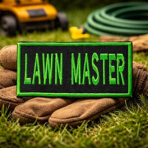 May include: A rectangular embroidered patch with a black background and a bright green border. The text LAWN MASTER is stitched in bright green capital letters across the center of the patch. The patch has a clean, finished edge design.