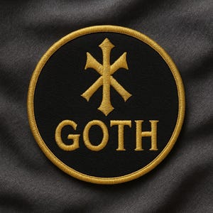 Puede incluir: Un parche negro y circular con un borde dorado y texto y diseño dorado bordado. La palabra "GOTH" está bordada en letras doradas en bloque debajo de un símbolo dorado. El parche está sobre un fondo de tela gris oscuro.
