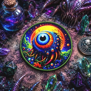 May include: A circular embroidered patch depicting a vibrant eye with a blue iris, set against a yellow moon and a starry backdrop. The patch is framed by a green border, with crystals, dice, and a jar with a cork surrounding it.