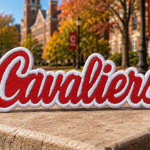 May include: A red and white embroidered patch featuring the word Cavaliers in a cursive script font. The patch has a thick white border outlining the red lettering, which is filled with dense red thread stitching throughout the entire design.