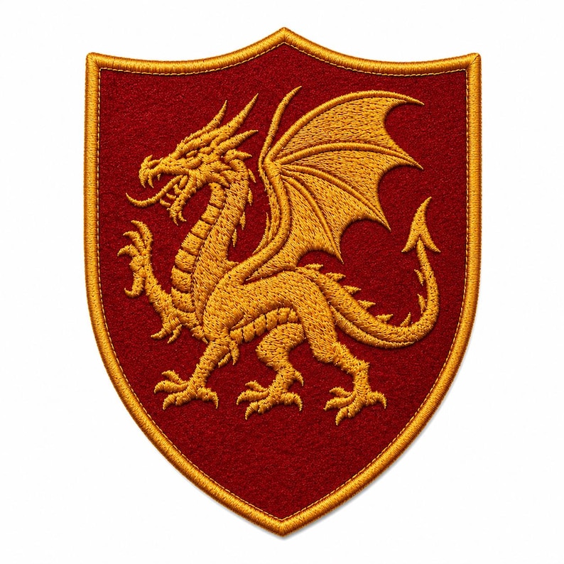 K&ouml;nnte beinhalten: Ein schildf&ouml;rmiger Stickaufn&auml;her mit einem goldenen Drachen auf einem dunkelroten Filzhintergrund. Der Drache ist im Profil mit ausgebreiteten Fl&uuml;geln, ausgestreckten Krallen und einem langen Schwanz dargestellt. Der Aufn&auml;her ist mit einem Goldfaden umrandet.