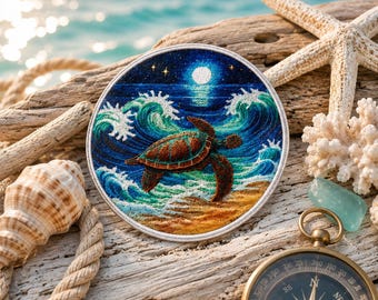 Op de afbeelding: Een ronde geborduurde patch met een zeeschildpad die zwemt in oceaangolven onder een sterrenhemel met volle maan. De patch is omgeven door schelpen, een zeester, koraal, een kompas en touw op een stuk drijfhout.