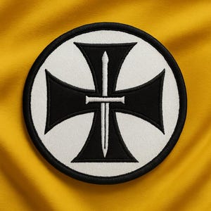 May include: Embroidered patch featuring a black cross with a sword in the center, set against a white background within a black-bordered circle. The patch is on a yellow fabric background.
