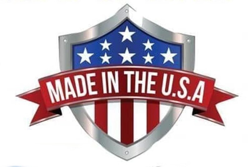 May include: A shield-shaped emblem featuring a blue field with white stars at the top and red and white vertical stripes at the bottom. A red ribbon banner overlays the center with the white text MADE IN THE U.S.A. in a bold, sans-serif font.