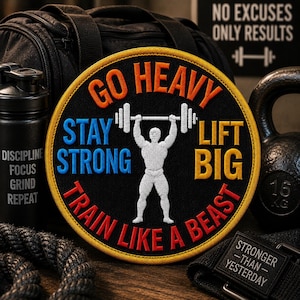 May include: A circular embroidered patch with a black background and a yellow border. It features a white silhouette of a person lifting a barbell overhead, surrounded by the text GO HEAVY, STAY STRONG, LIFT BIG, and TRAIN LIKE A BEAST in colors.