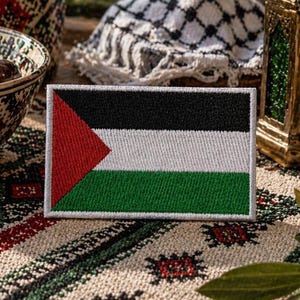 Op de afbeelding: Een rechthoekige geborduurde patch met de vlag van Palestina. Het ontwerp bestaat uit drie horizontale banen in zwart, wit en groen, met een rode driehoek aan de linkerzijde. De patch is afgewerkt met een witte gestikte rand rondom.