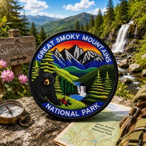 May include: A circular embroidered patch featuring a black bear, green pine trees, a blue waterfall, and jagged mountains under a sunset sky. The text reads Great Smoky Mountains National Park in white letters against a dark blue border.