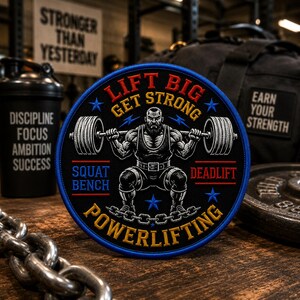 May include: A circular embroidered patch featuring a black background with a central illustration of a bearded athlete performing a barbell squat. The text reads LIFT BIG GET STRONG, SQUAT BENCH, DEADLIFT, and POWERLIFTING in red, yellow, and blue.
