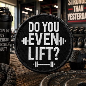 May include: A circular black embroidered patch featuring the white text DO YOU EVEN LIFT? centered between two white barbell icons. The patch has a thick black stitched border and is displayed against a dark, textured wooden surface.