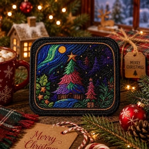 May include: A rectangular embroidered patch featuring a vibrant Christmas tree with a star topper, surrounded by a dark night sky with aurora borealis, smaller trees, and stars, all framed by a thick black border with gold stitching.