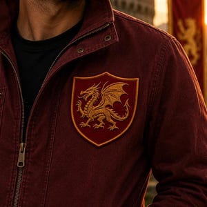 K&ouml;nnte beinhalten: Eine dunkelrote Jacke mit Stehkragen, Metallrei&szlig;verschluss und einem auff&auml;lligen gestickten Aufn&auml;her auf der Brust. Der schildf&ouml;rmige Aufn&auml;her hat einen dunkelroten Hintergrund und zeigt einen detaillierten goldenen Drachen.