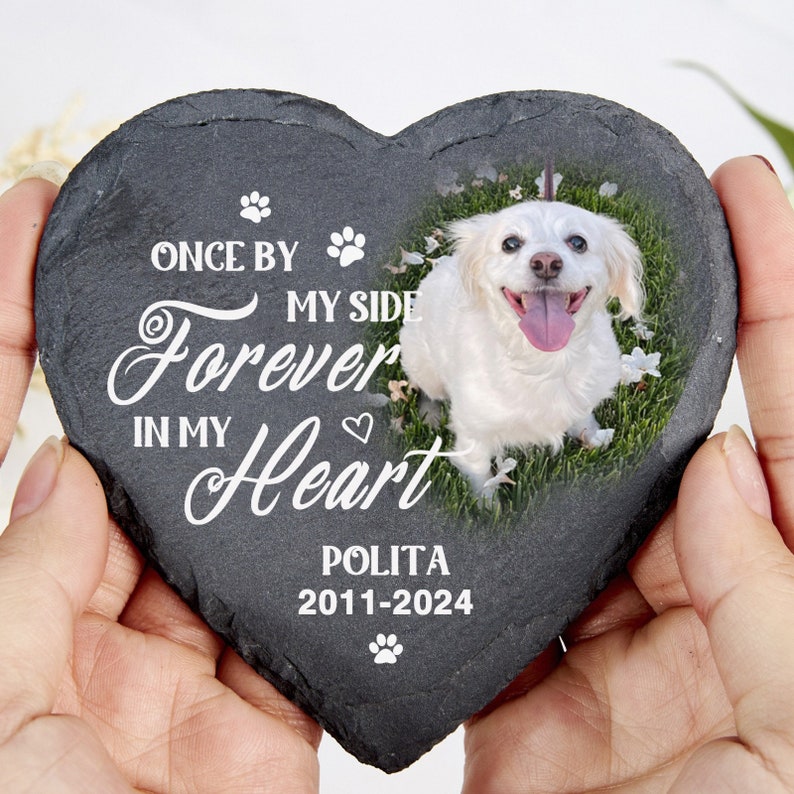 May include: Heart-shaped slate pet memorial featuring a white dog on grass. The memorial has the text "Once by my side, forever in my heart" and the name "Polita" with the years 2011-2024.