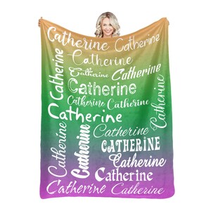 May include: A soft, colorful fleece blanket with the name "Catherine" repeated in white lettering on a gradient background of yellow, green, and purple.