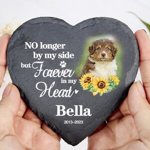 May include: Heart-shaped slate memorial stone featuring a puppy photo and sunflowers. The text says "NO longer by my side but Forever in my Heart", with the name "Bella" and dates "2013-2023".