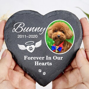 May include: A heart-shaped, dark grey slate memorial stone with the name "Bunny" and dates 2011-2020 in white script. It features a photo of a brown dog and the text "Forever In Our Hearts". Includes paw prints and angel wings.