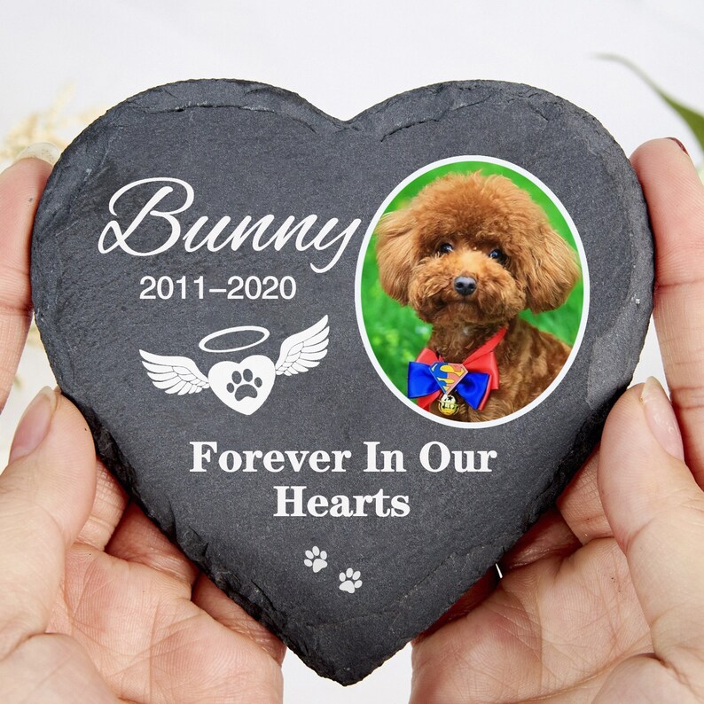 May include: A heart-shaped, dark grey slate memorial stone with the name "Bunny" and dates 2011-2020 in white script. It features a photo of a brown dog and the text "Forever In Our Hearts". Includes paw prints and angel wings.