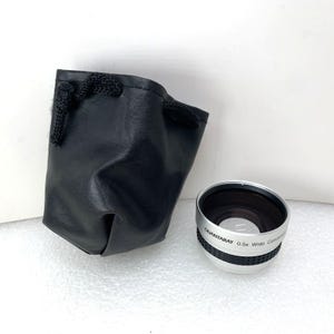 May include: A silver and black Quantaray 0.5x Wide Converter lens with a black leather drawstring pouch. The lens has black text that reads "QUANTARAY 0.5x Wide Converter". The pouch is made of black leather and has a black drawstring closure.