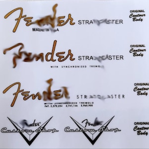 May include: A white sheet featuring Fender Stratocaster and Custom Shop logos. The Fender logos are gold, with text including "Original Contour Body" and patent numbers.