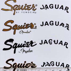 May include: Four different versions of a Squier Jaguar guitar logo. The logos are in black and gold, with the text "Squier" and "Jaguar" in a stylized font. The logos are printed on a white background.