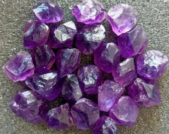 Peut inclure: Une collection de cristaux d'améthyste bruts de différentes tailles et formes. Les cristaux sont d'une couleur violet foncé et ont une texture naturelle et rugueuse.