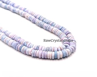 May include: A strand of small, flat, circular beads in shades of pale blue, lavender, and white. The beads are arranged in a continuous row, displaying a smooth, matte texture. The text RawCrystalsIndia is visible on the right side of the image.
