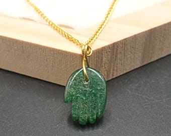Könnte beinhalten: Eine goldene Kettenkette mit einem grünen Hamsa-Hand-Anhänger. Der Anhänger ist aus einem glatten, grünen Stein mit leicht strukturierter Oberfläche gefertigt.