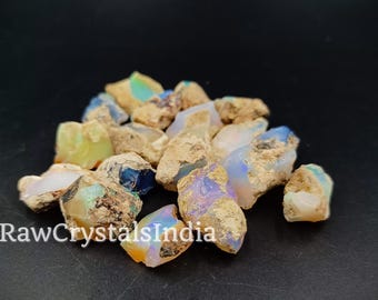 Puede incluir: Una colección de cristales de ópalo en bruto en varios tonos de blanco, azul y verde. Los cristales son ásperos y tienen un aspecto natural y terroso.