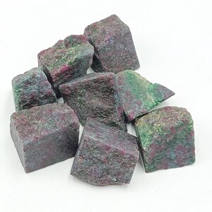 Könnte beinhalten: Eine Ansammlung roher Rubinsteine mit einer Mischung aus roten, grünen und grauen Farbtönen. Die ungeschliffenen Edelsteine haben unregelmäßige Formen und eine strukturierte Oberfläche, ideal für Schmuckherstellung oder Sammlungen.