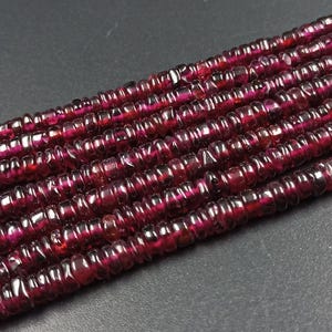 May include: A strand of deep red gemstone beads, each bead is faceted and has a slightly irregular shape. The beads are strung together to create a long necklace or bracelet.
