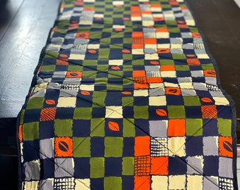 Peut inclure: Un chemin de table matelassé avec un motif à carreaux en noir, vert, orange et crème. Le motif présente de petits motifs de feuilles.