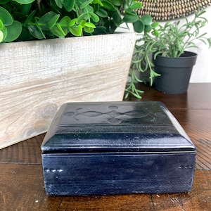 May include: A dark blue leather box with an intricate design on the lid. The box is closed and sitting on a wooden surface.