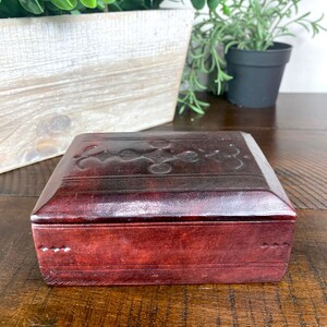 May include: A small, rectangular, brown leather box with an intricate floral design embossed on the top. The box has a hinged lid and is made of high-quality leather.