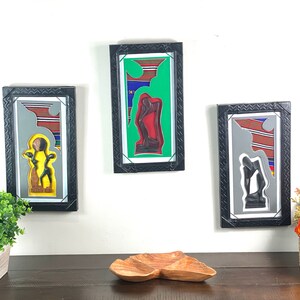 May include: Three framed black and white art prints with colorful geometric patterns and wooden sculptures of people. The frames are black with a textured border.