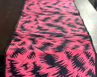 Peut inclure: Un chemin de table rose et noir avec un motif géométrique. Le chemin de table est matelassé et a une bordure noire.