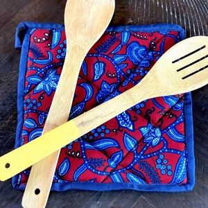 May include: Two wooden spoons, one with a yellow handle, on a red and blue patterned kitchen hot pad.
