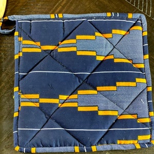 May include: A blue and orange quilted hot pad with a geometric pattern. The hot pad has a loop for hanging.