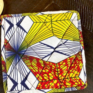 May include: A white quilted hot pad with a geometric pattern in red, yellow, and blue. The pattern is made up of squares and triangles.